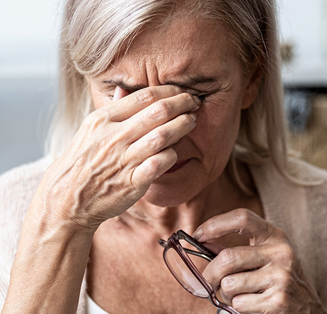 mujer de edad frotando sus ojos mientras sostiene sus gafas